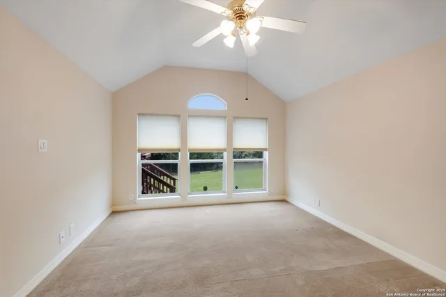 an empty room with chandelier fan and windows