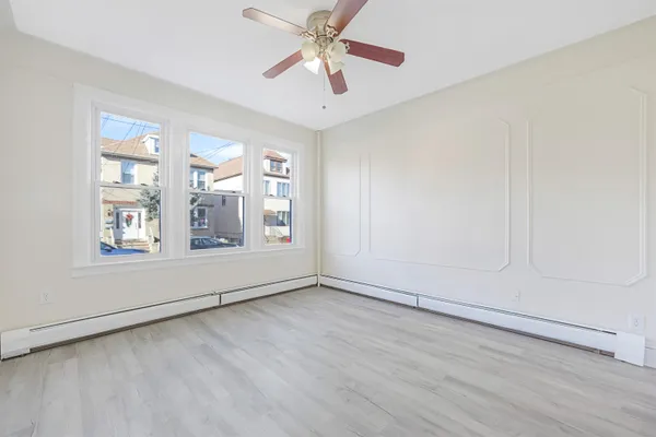 an empty room with wooden floor chandelier fan and windows