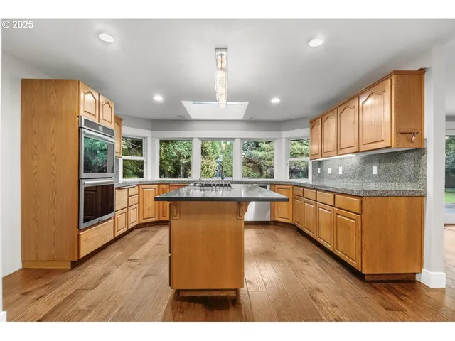 a kitchen with stainless steel appliances granite countertop wooden cabinets a refrigerator a sink a stove and a wooden floors