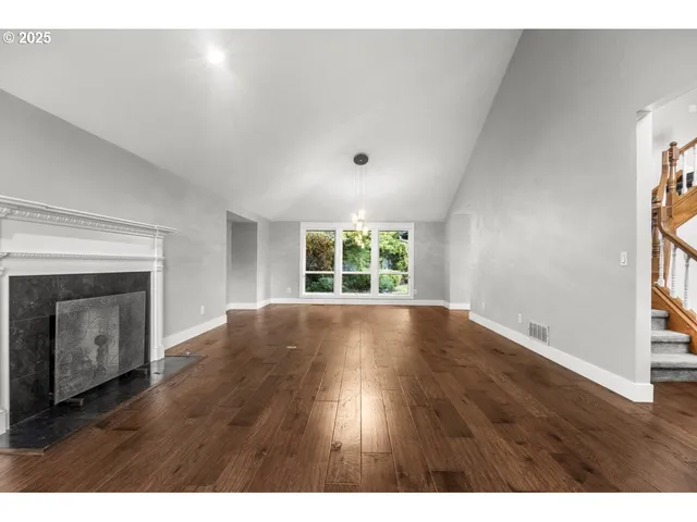 a view of an empty room with wooden floor fireplace and a window