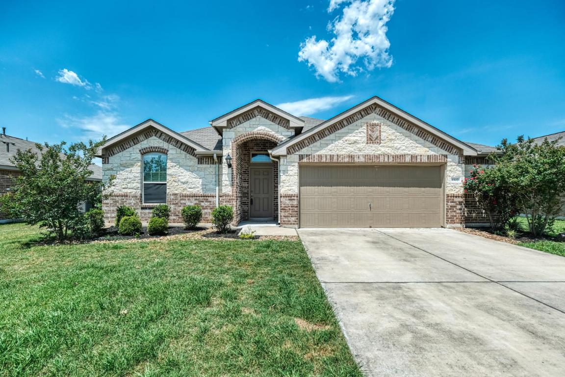 View of front facade with stone siding, brick siding, driveway, a garage, and a front yard
