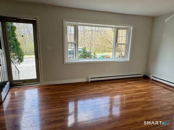 a view of an empty room with wooden floor and a window