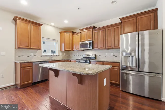 a kitchen with stainless steel appliances granite countertop a refrigerator a sink dishwasher a stove and white countertops with wooden floor