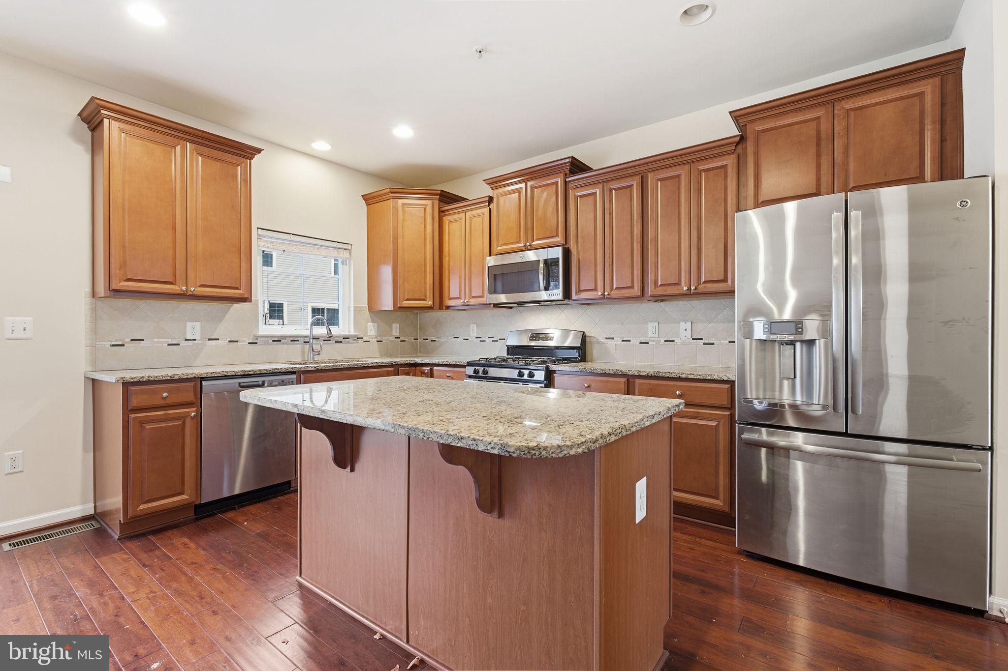 7025 Southmoor Street Hanover, MD 21076 - Photo 14 of 35 a kitchen with stainless steel appliances granite countertop a refrigerator a sink dishwasher a stove and white countertops with wooden floor