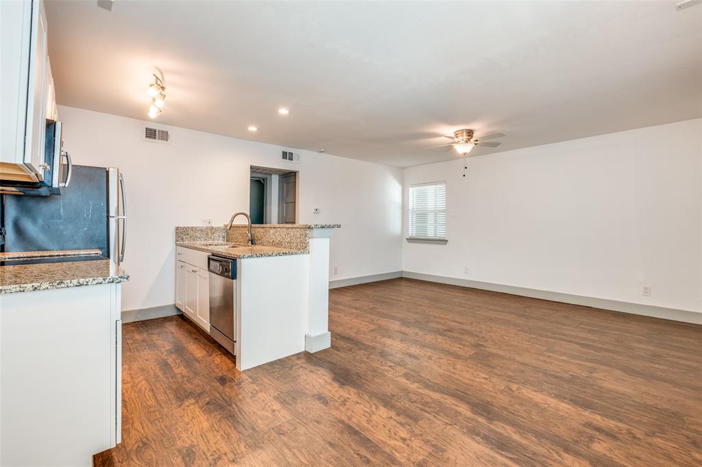 4633 Fairmount Street, Unit 109 Dallas, TX 75219 - Photo 7 of 14 Kitchen and living area featuring wood-finish flooring, white cabinetry, granite countertops, and stainless steel appliances