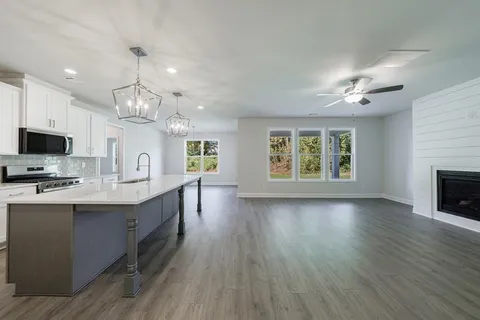 an empty room with wooden floor a ceiling fan a fireplace and windows