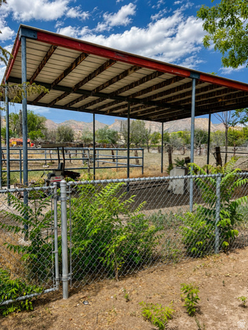 1766 Kenilworth Road Spring Glen, UT 84526 - Photo 20 of 24 Metal-framed open-air structure featuring a sloped roof, chain-link fencing, and a surrounding landscape of mature trees and distant mountains