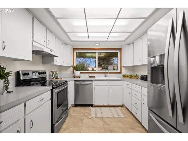 a kitchen with stainless steel appliances granite countertop a sink a stove a refrigerator cabinets and a window