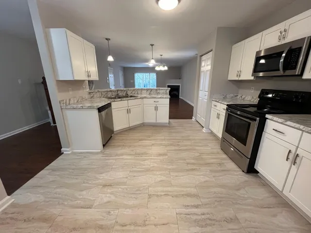 a large white kitchen with stainless steel appliances granite countertop a stove a sink dishwasher and a microwave oven with wooden floor