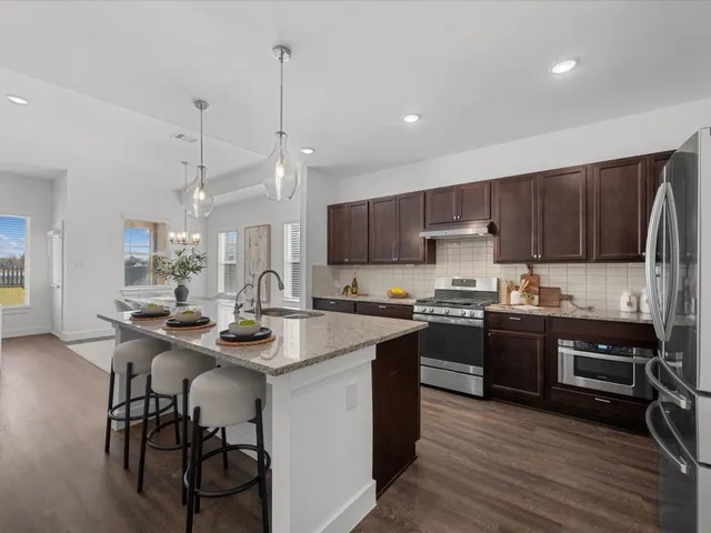 a kitchen with stainless steel appliances granite countertop wooden cabinets a stove a sink a stove a dining table and chairs