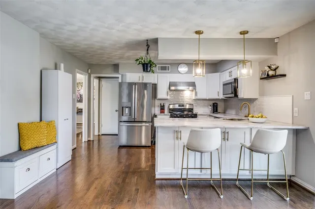 a kitchen with stainless steel appliances granite countertop a refrigerator a stove a sink and white cabinets with wooden floor