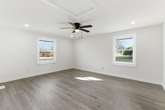an empty room with wooden floor ceiling fan and windows