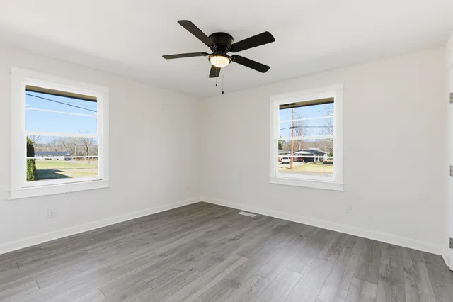 an empty room with wooden floor ceiling fan and windows