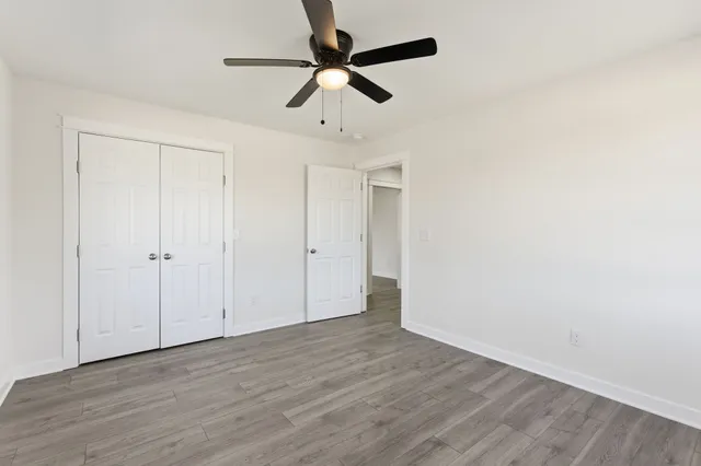 an empty room with wooden floor fan and windows