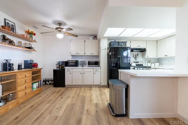 a kitchen with granite countertop a refrigerator a sink dishwasher a stove and white cabinets with wooden floor