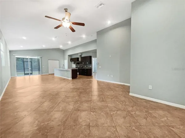 an empty room with ceiling fan and kitchen view