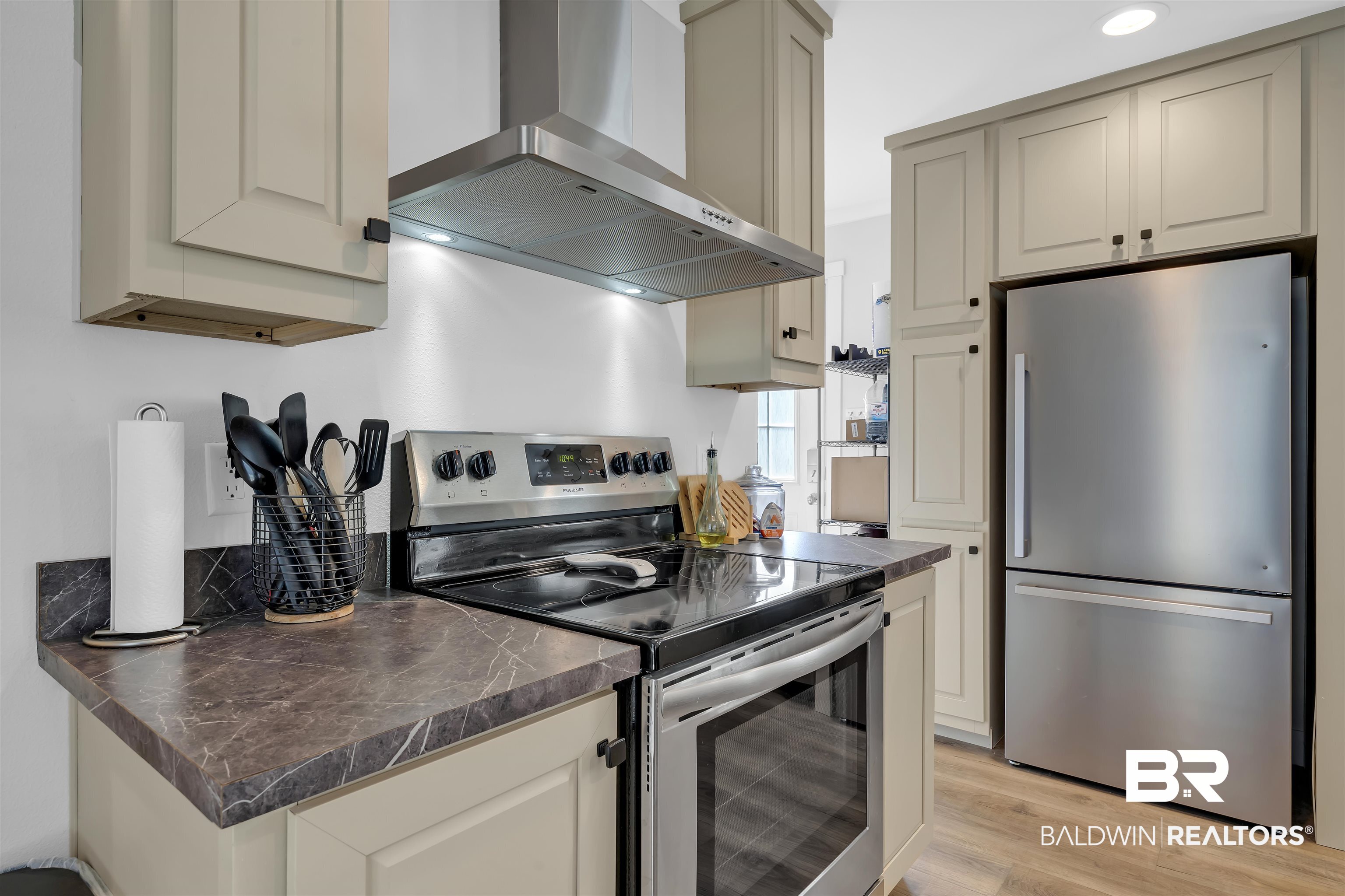 16707 Fort Morgan Road Gulf Shores, AL 36542 - Photo 6 of 22 Kitchen featuring stainless steel appliances, wall chimney range hood, dark countertops, light wood finished floors, and cream cabinets