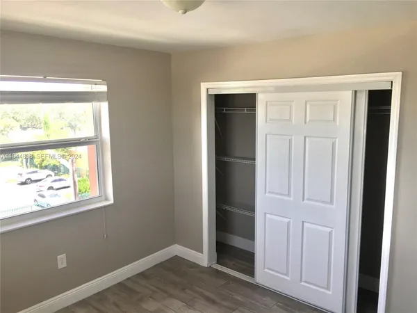 an empty room with wooden floor closet and windows