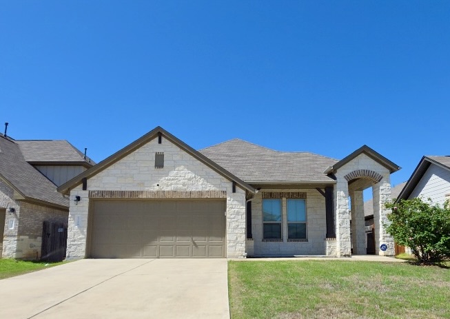 French country inspired facade featuring a garage, stone siding, driveway, and a front yard