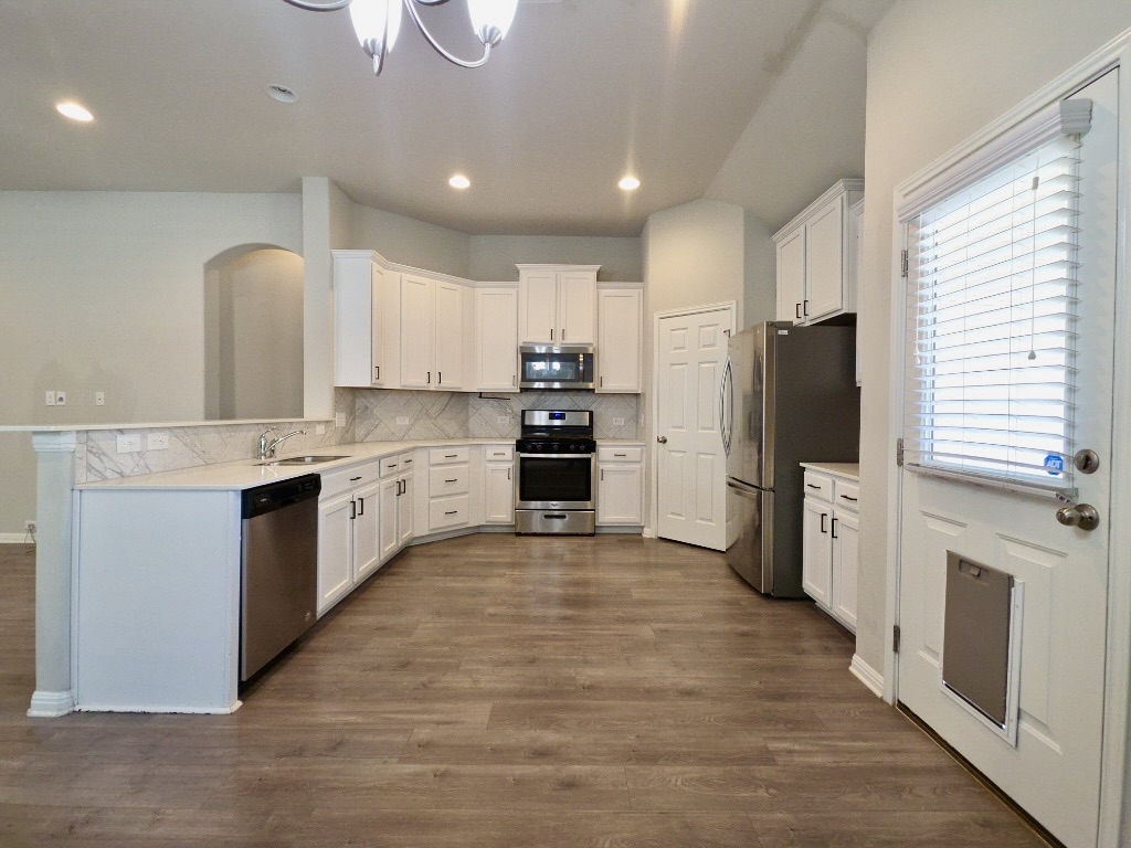 13208 Mariscan Street Manchaca, TX 78652 - Photo 5 of 31 Kitchen with stainless steel appliances, white cabinetry, dark wood-style flooring, decorative backsplash, and a peninsula.