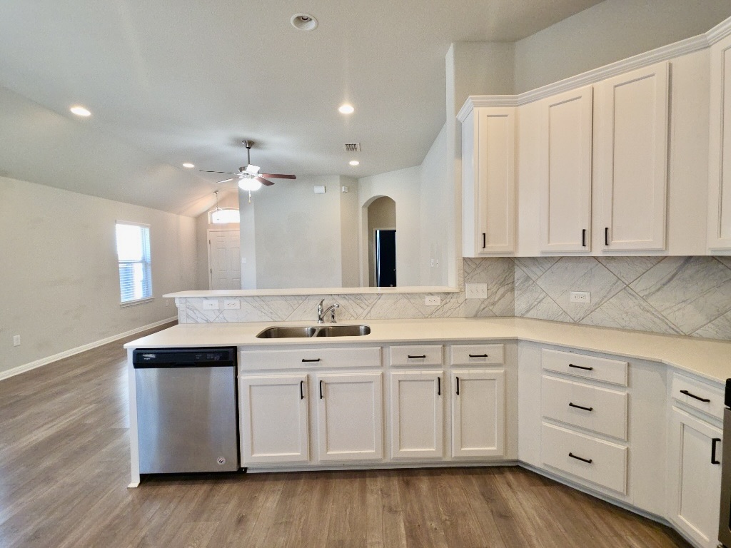 13208 Mariscan Street Manchaca, TX 78652 - Photo 6 of 31 Kitchen with dishwasher, lofted ceiling, white cabinetry, decorative backsplash, and a peninsula.