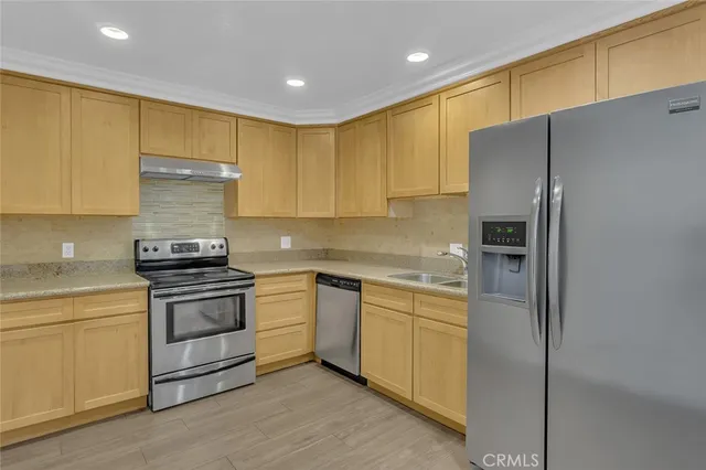 a kitchen with stainless steel appliances granite countertop a refrigerator a sink dishwasher a stove and white cabinets with wooden floor