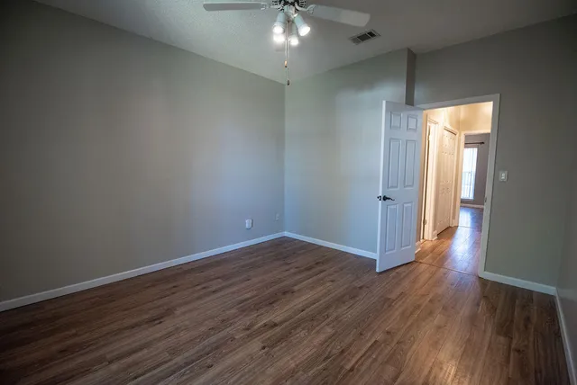 an empty room with wooden floor chandelier fan and windows