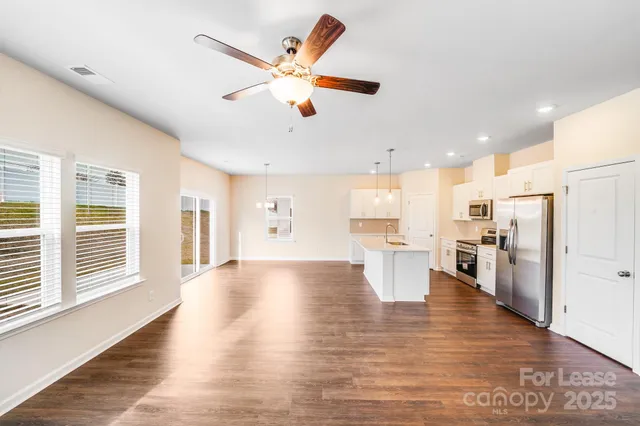 a view of an empty room and kitchen with wooden floor