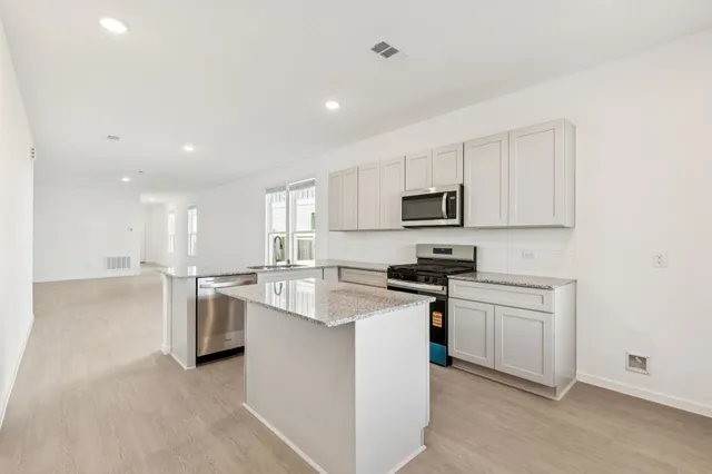 a kitchen with stainless steel appliances granite countertop a stove top oven a sink a refrigerator and white cabinets