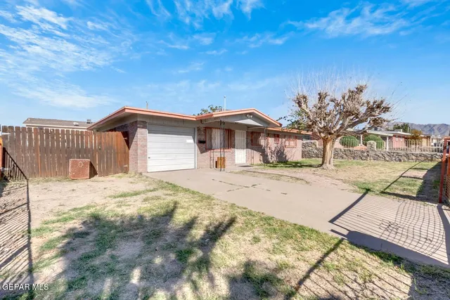 a front view of a house with a dirt yard and a large tree