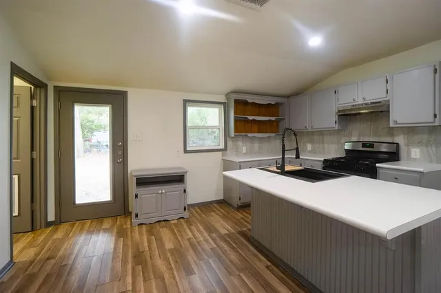 a kitchen with a sink a stove cabinets and wooden floor