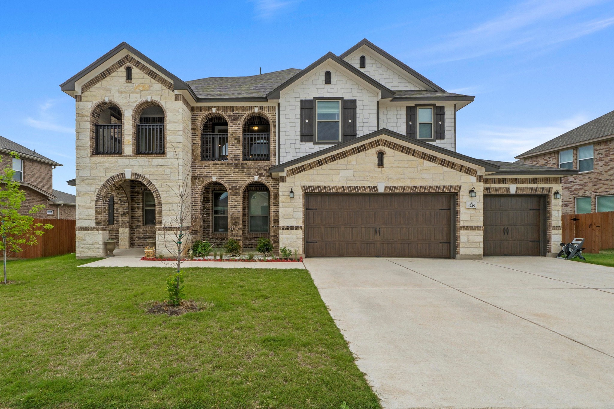 Exterior featuring stone and brick accents, decorative arched windows, two second-story balconies, and a three-car garage