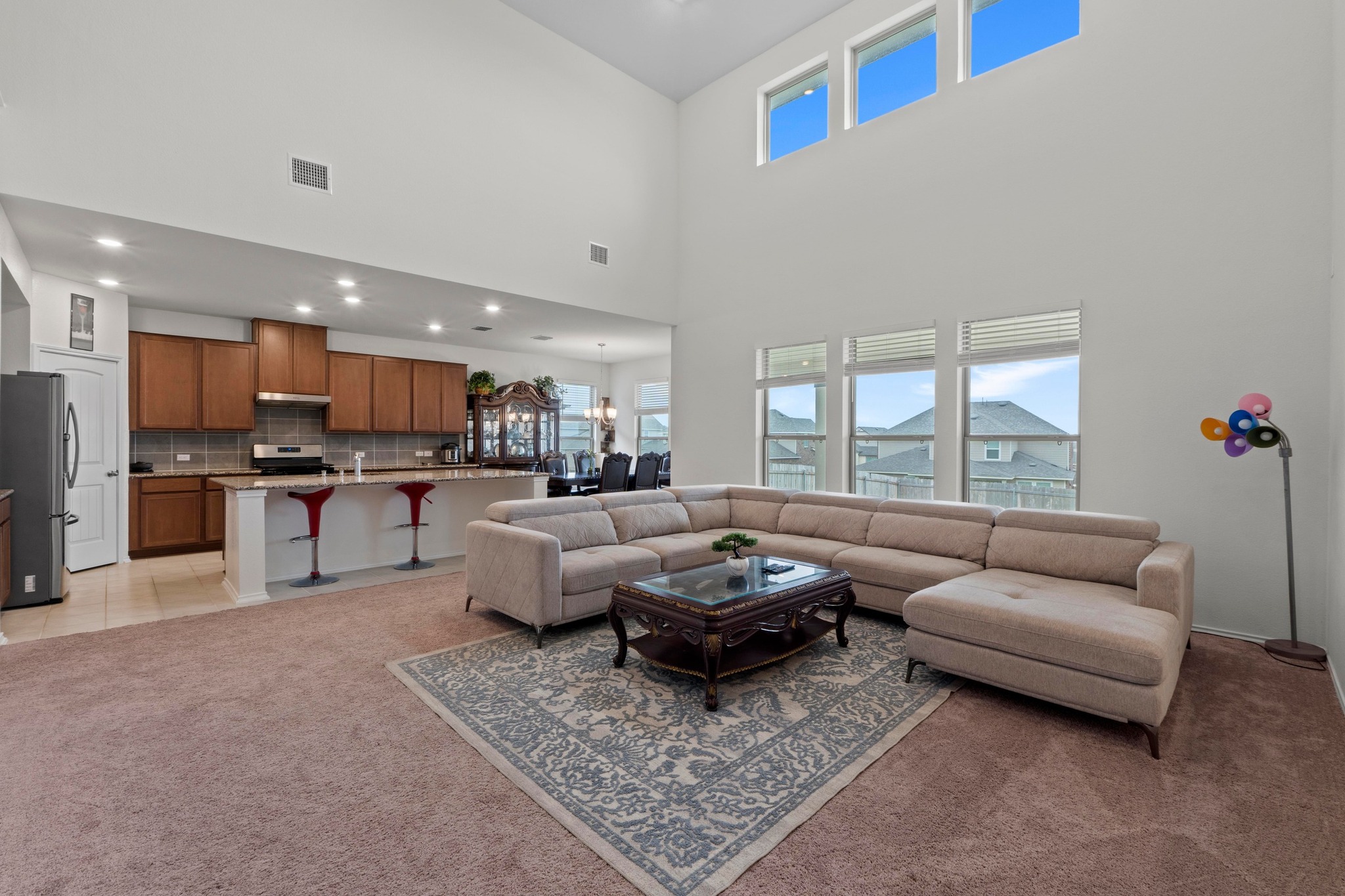 4729 San Rufo Drive Round Rock, TX 78665 - Photo 5 of 36 Open-concept living area with a two-story ceiling, abundant natural light, and a kitchen featuring wood-finish cabinetry, stainless steel appliances, and a tiled backsplash