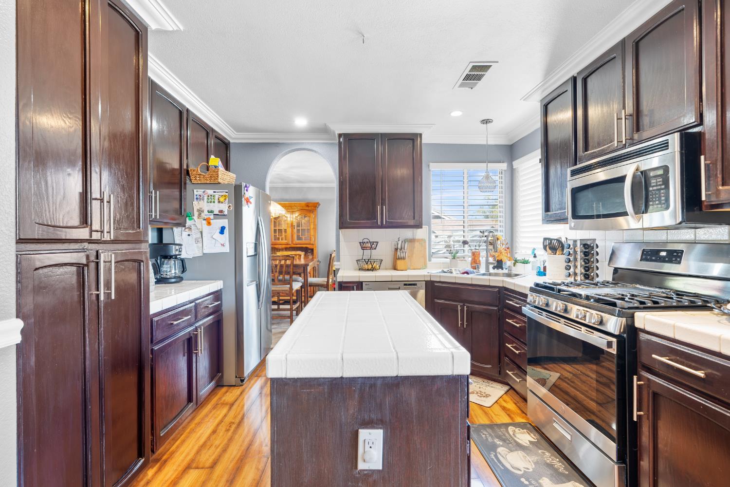 446 Port Street Los Banos, CA 93635 - Photo 15 of 55 Dark Wood Cabinetry, Crown Molding, Wood Plank Style Vinyl Flooring, Tile Counter Space, Stainless Steel Appliances, Gas Stove & Oven.