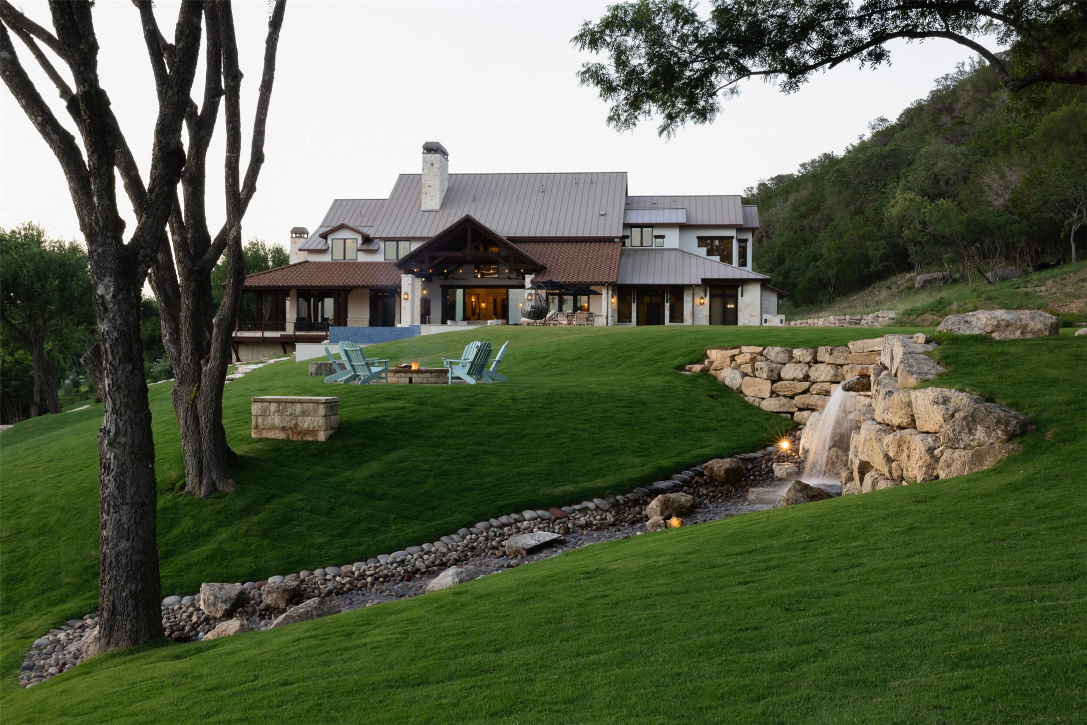 15016 Flat Top Ranch Road Austin, TX 78732 - Photo 7 of 40 Rear view of house with a lawn, a fire pit, a patio, a chimney, and a metal roof