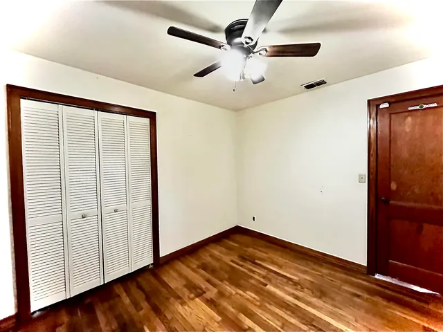 an empty room with wooden floor closet and windows
