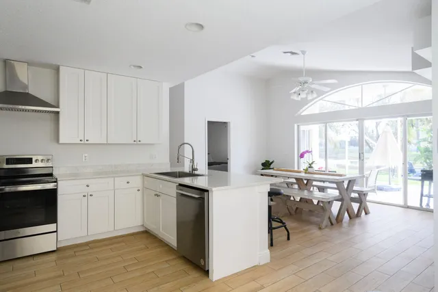 a kitchen with stainless steel appliances granite countertop white cabinets a stove a sink and a dining table with wooden floor