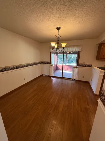 a view of a refrigerator in kitchen and an empty room with wooden floor