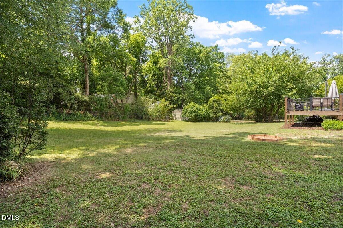 1404 Ivy Lane Raleigh, NC 27609 - Photo 34 of 37 Expansive grassy yard with mature perimeter trees, a raised wood deck, and a wood-framed ground-level feature