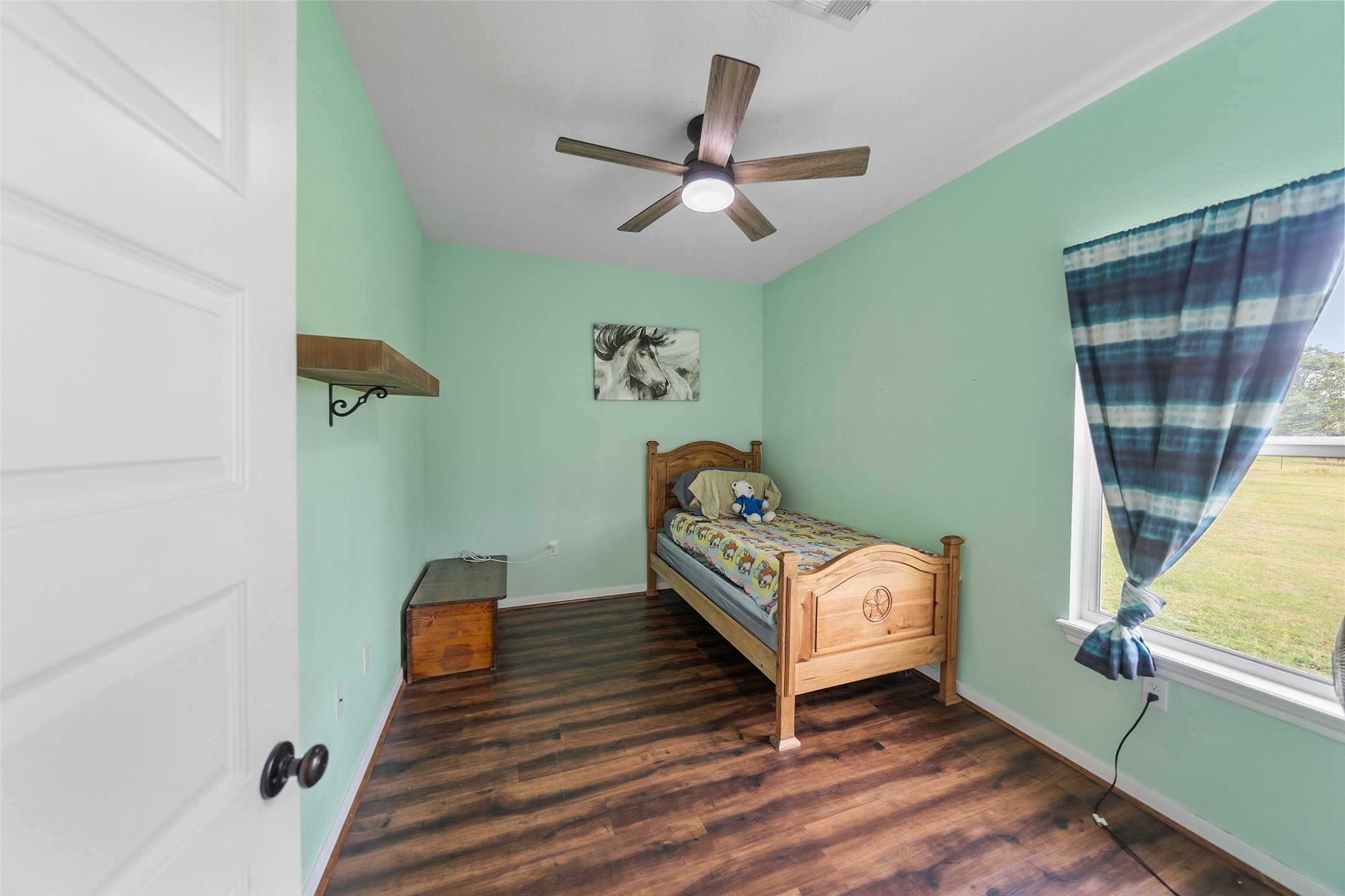 1121 Pelican Road Shepherd, TX 77371 - Photo 21 of 34 Cozy secondary bedroom with wood-look flooring, ceiling fan, and a large window bringing in natural light and peaceful outdoor views.
