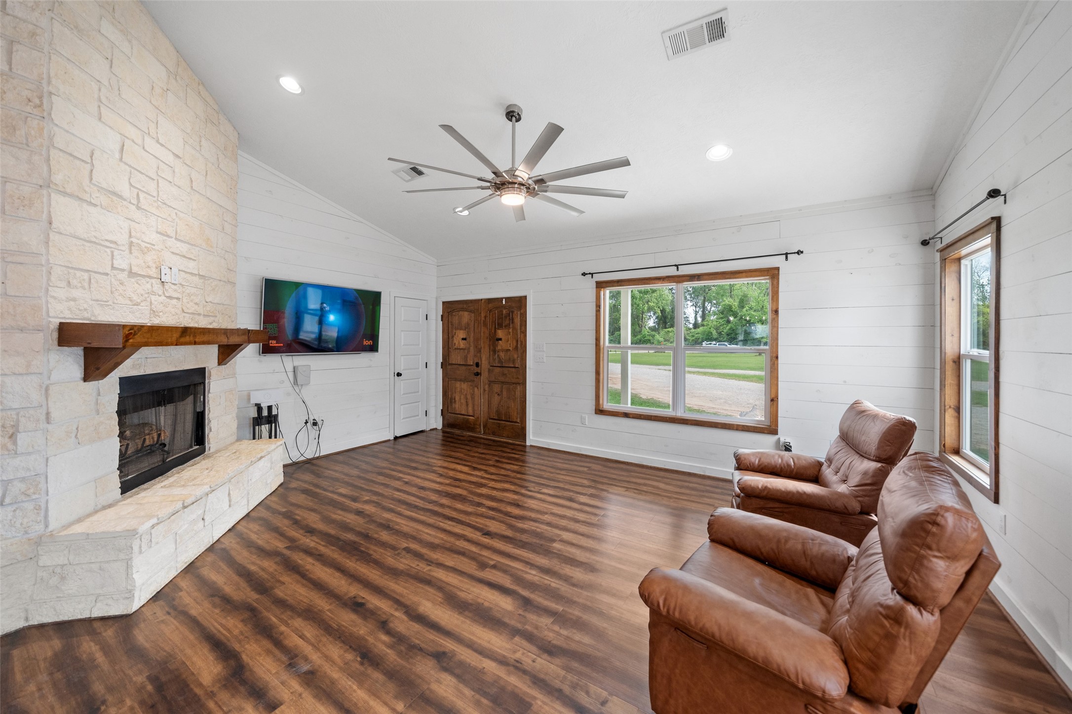 1121 Pelican Road Shepherd, TX 77371 - Photo 5 of 34 Bright, open living area featuring wood-look flooring, shiplap walls, a stone fireplace, and large windows that bring in natural light and scenic views.