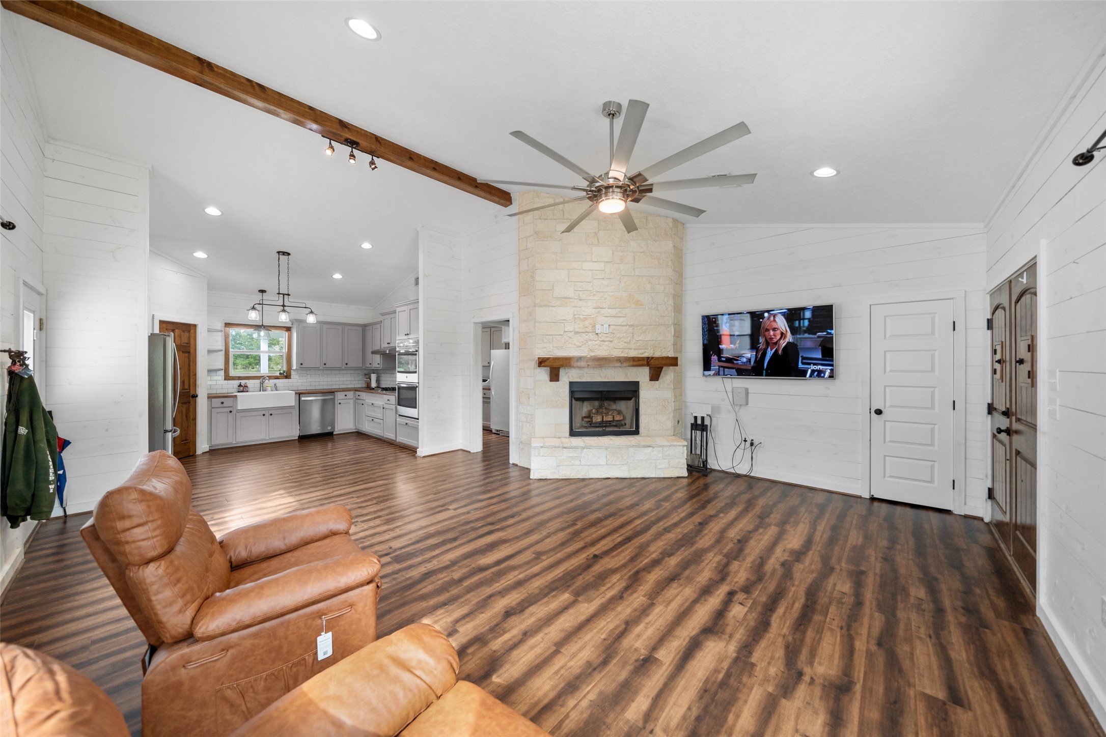 1121 Pelican Road Shepherd, TX 77371 - Photo 10 of 34 Spacious open-concept layout seamlessly connecting the living area and kitchen, highlighted by wood-look flooring, exposed beam, and a striking stone fireplace as the focal point.