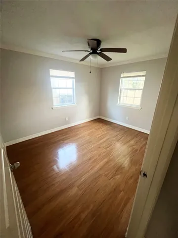 an empty room with wooden floor ceiling fan and windows