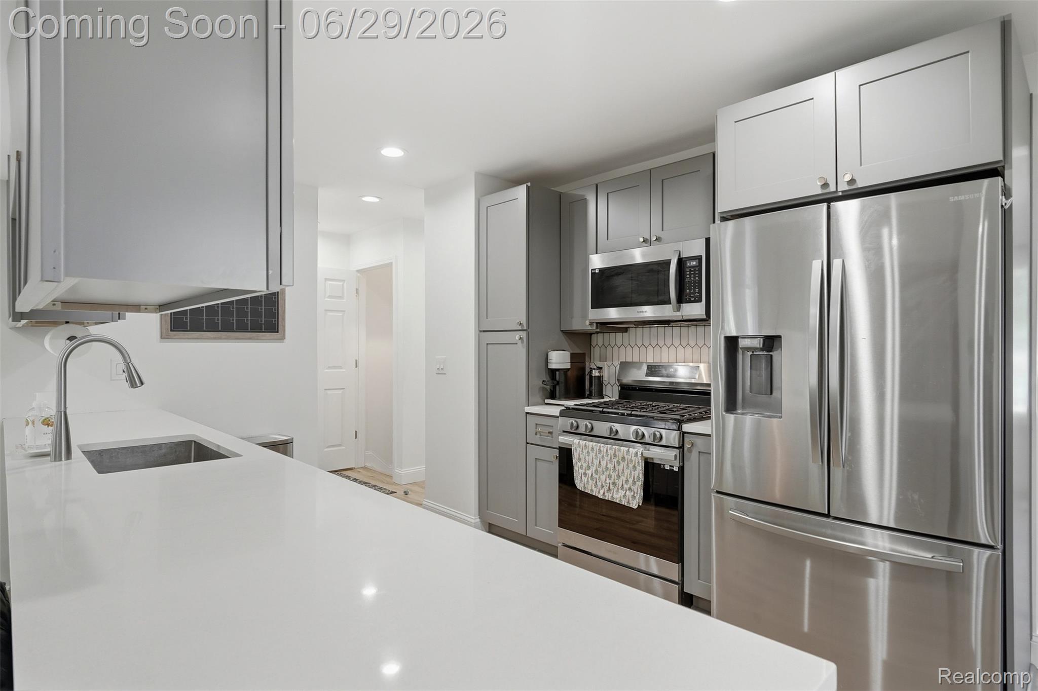 45179 Rudgate Road Canton, MI 48188 - Photo 11 of 48 Kitchen showcasing light gray cabinetry, stainless steel appliances, a white solid surface countertop, an undermount sink with a gooseneck faucet, and a patterned tile backsplash