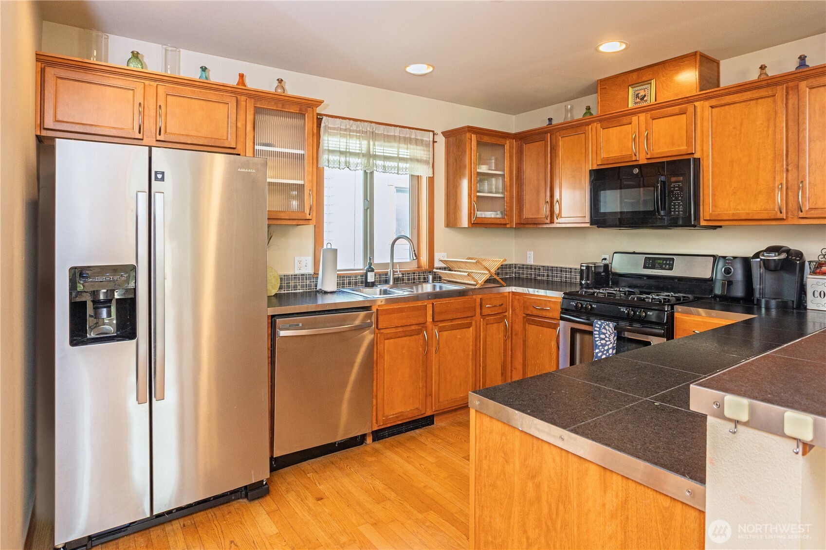 3314 Wetmore Avenue South, Unit B Seattle, WA 98144 - Photo 9 of 28 a kitchen with stainless steel appliances granite countertop a refrigerator a sink dishwasher a stove and a dining table with wooden floor