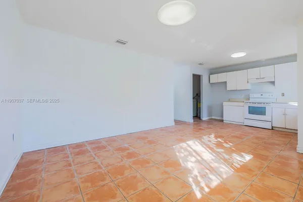 a view of an empty room with kitchen and a window