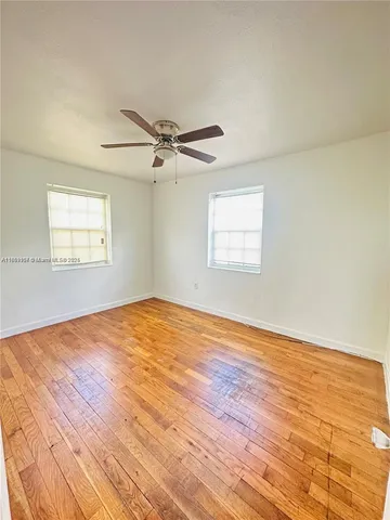 an empty room with wooden floor fan and windows