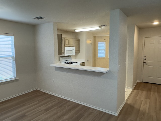109 Plover Pass Georgetown, TX 78633 - Photo 18 of 25 Kitchen featuring wood finished floors, light countertops, white appliances, a peninsula, and a kitchen breakfast bar