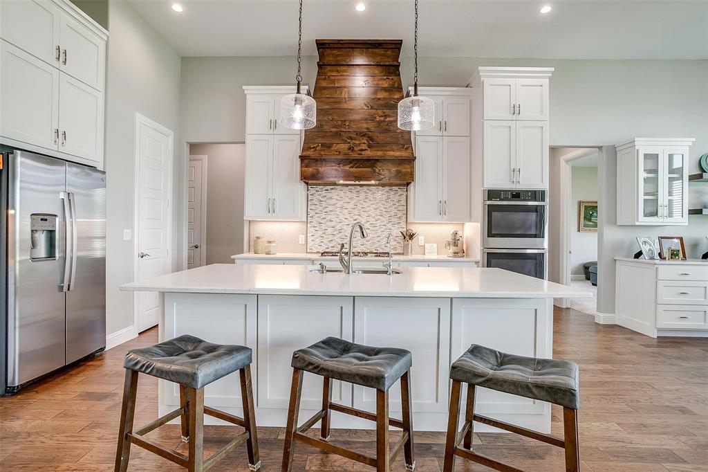 7730 Barber Rnch Road Fort Worth, TX 76126 - Photo 11 of 19 Kitchen featuring a central island with countertop seating, white shaker-style cabinetry, stainless steel appliances, a wood-finish range hood, and wood-finish flooring