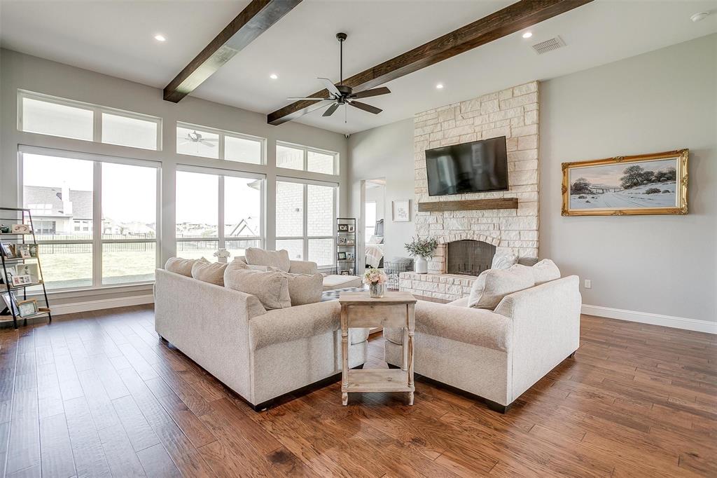 7730 Barber Rnch Road Fort Worth, TX 76126 - Photo 5 of 19 Bright living room featuring a stone fireplace, wood-finish flooring, high ceilings with exposed wood beams, and a ceiling fan